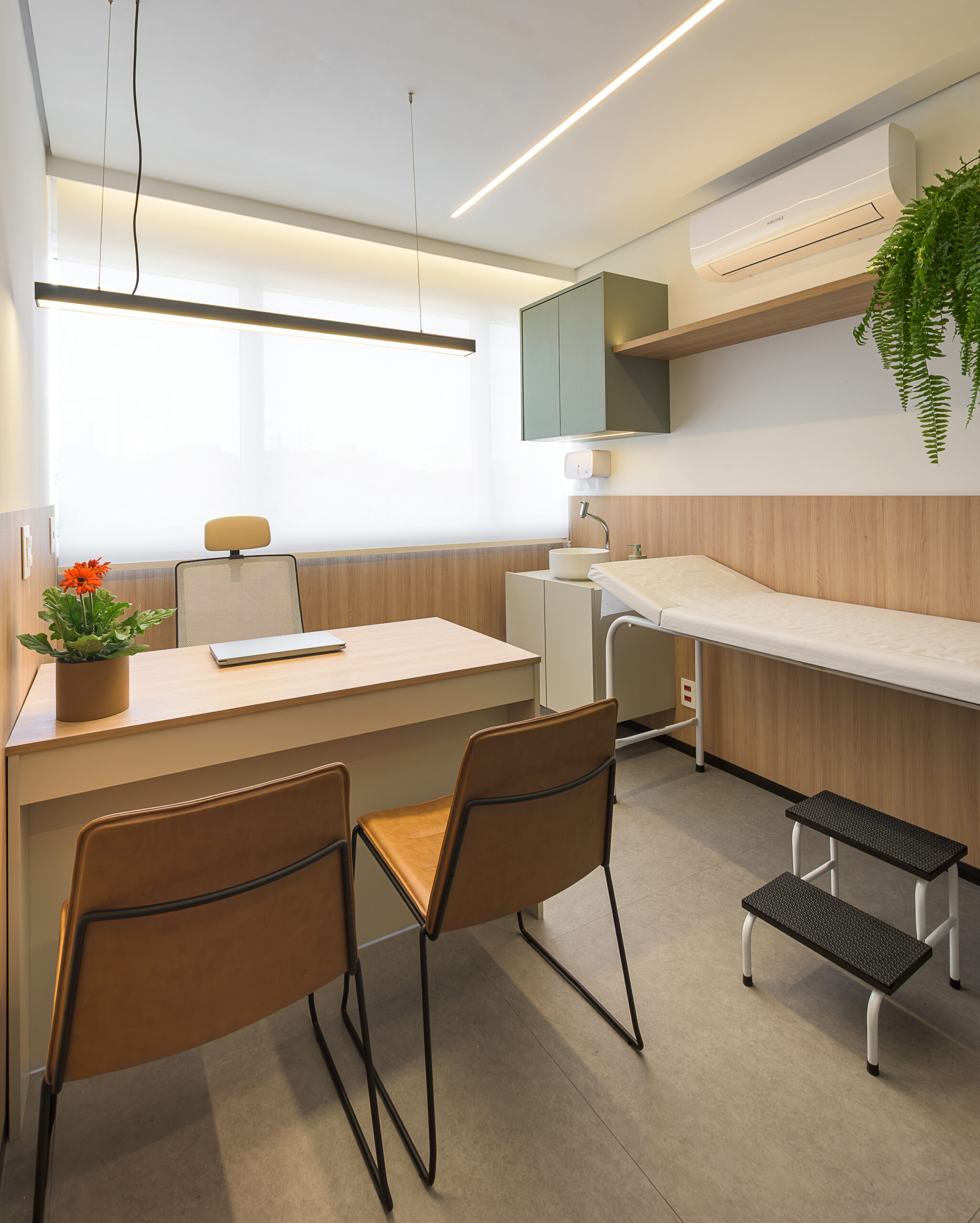 Consultório com mesa de atendimento, maca, lavatório e iluminação linear do consultório de cardiologia — projeto e obra da MWARQ