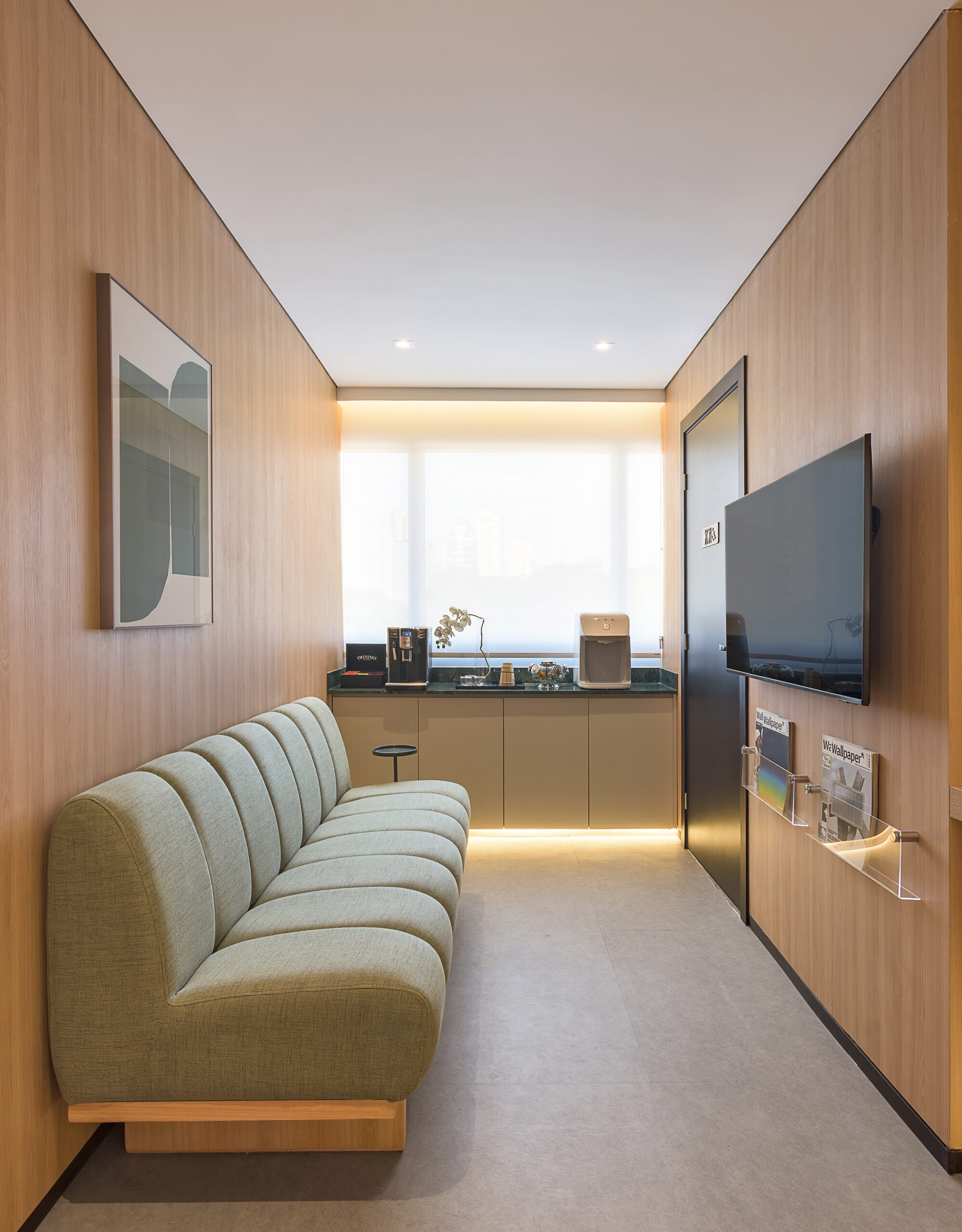 Sala de espera com sofá verde, painel de madeira e copa do consultório de cardiologia — projeto e obra da MWARQ