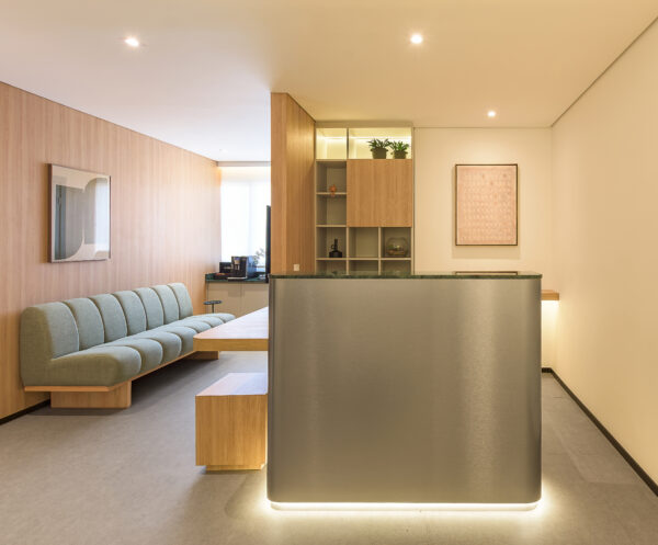 Balcão de recepção em inox escovado com iluminação no rodapé e sala de espera ao fundo do consultório de cardiologia — projeto e obra da MWARQ